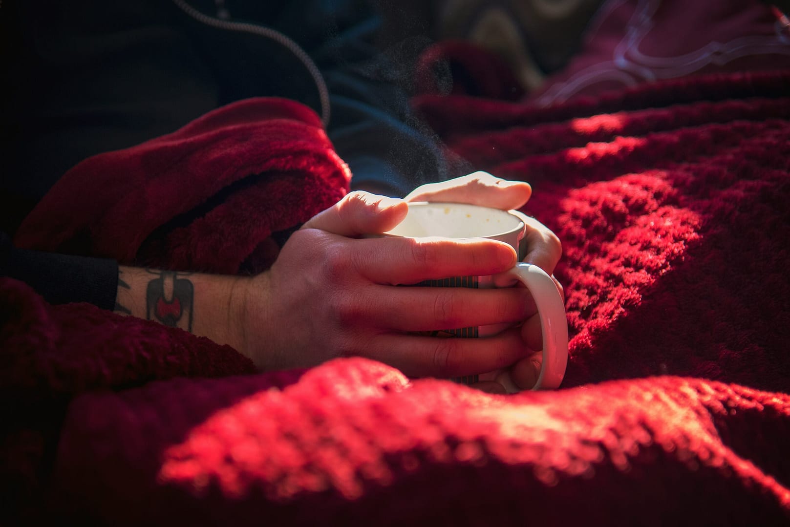 Hands holding cup while wrapped in blanket