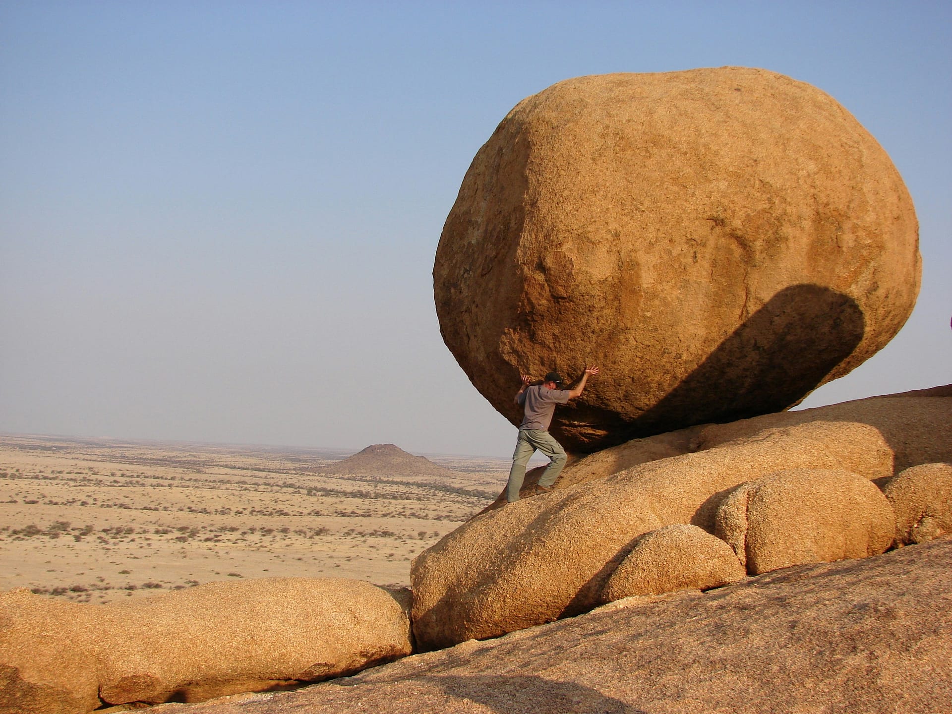 Man pushing holding huge rock in the desert
